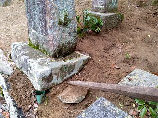 墓石の傾きを修正する為に低い側の石をバールで持ち上げる